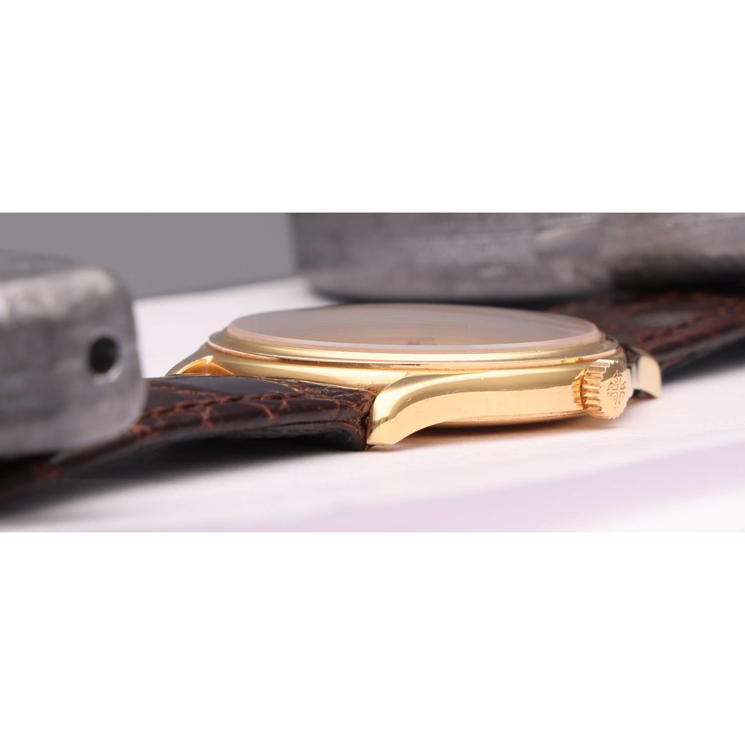 Close-up of a gold wristwatch with a brown leather strap lying on its side on a white surface.