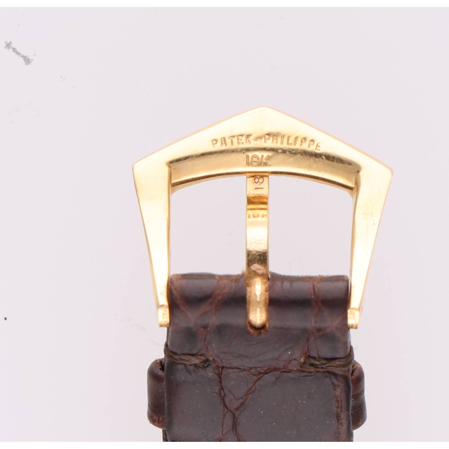 Gold-toned watch buckle engraved with 'PATEK PHILIPPE' and '18K' on a brown leather strap, close-up view.