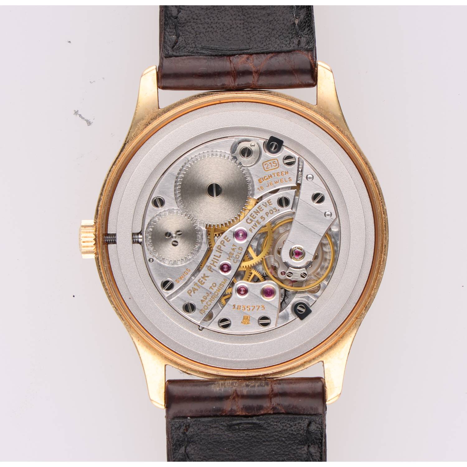Close-up of a gold-cased mechanical wristwatch movement with gears and jewels visible through the back plate.