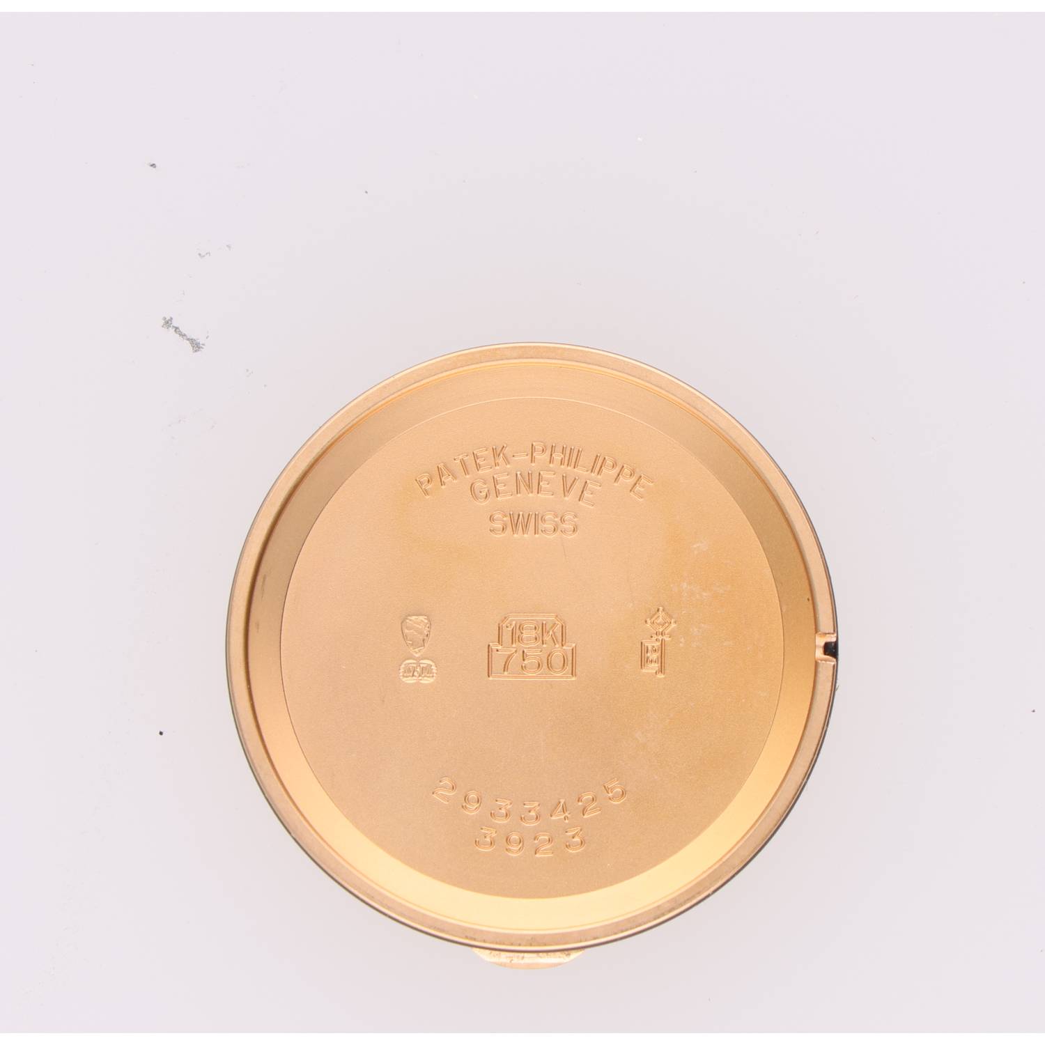 Gold circular watch case back with engravings reading 'Patek-Philippe Geneve Swiss' and '18K 750' along with serial numbers on a white surface.