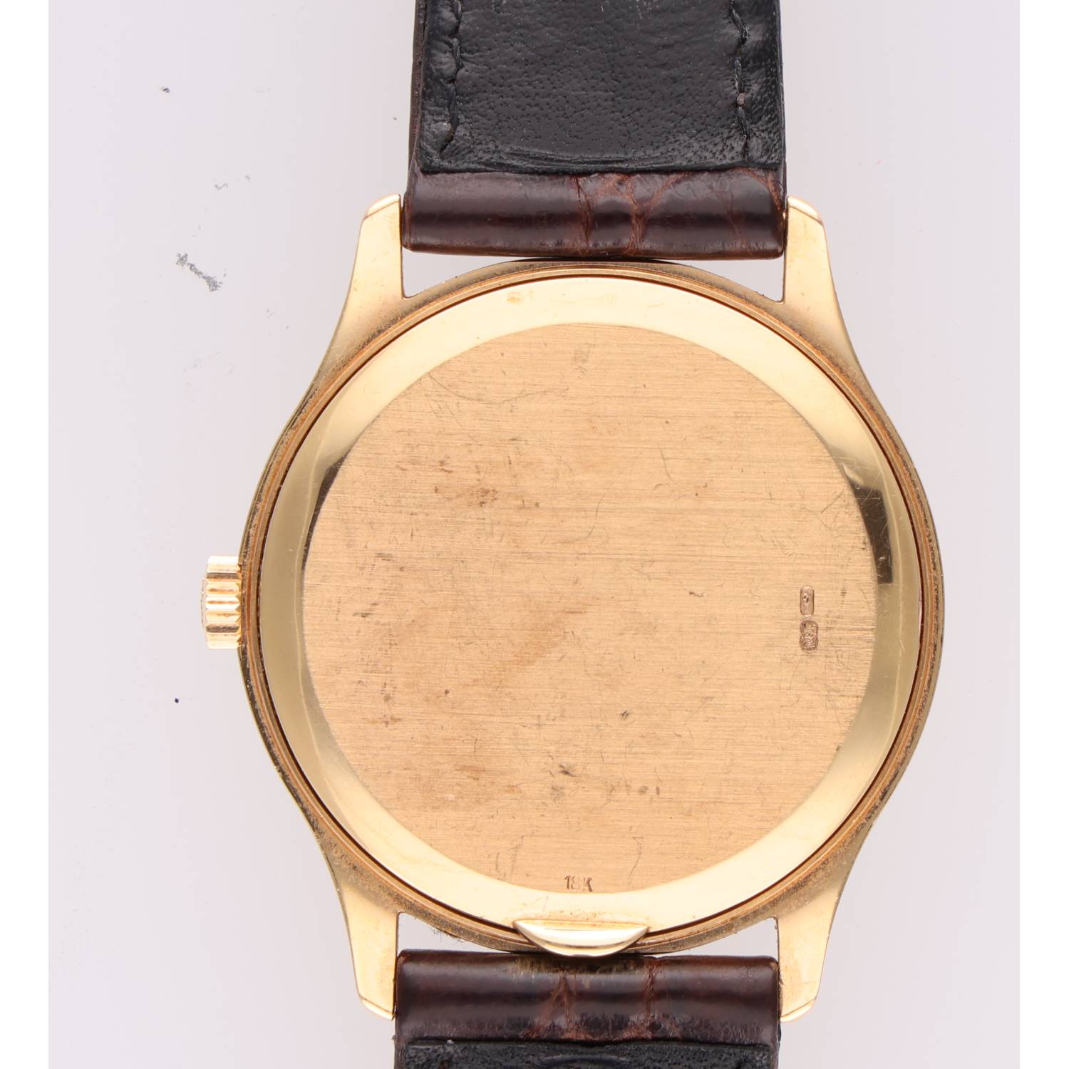 Gold-tone wristwatch viewed from the back, with a worn leather strap; visible scratches on the case and an 18K stamp near the bottom edge.