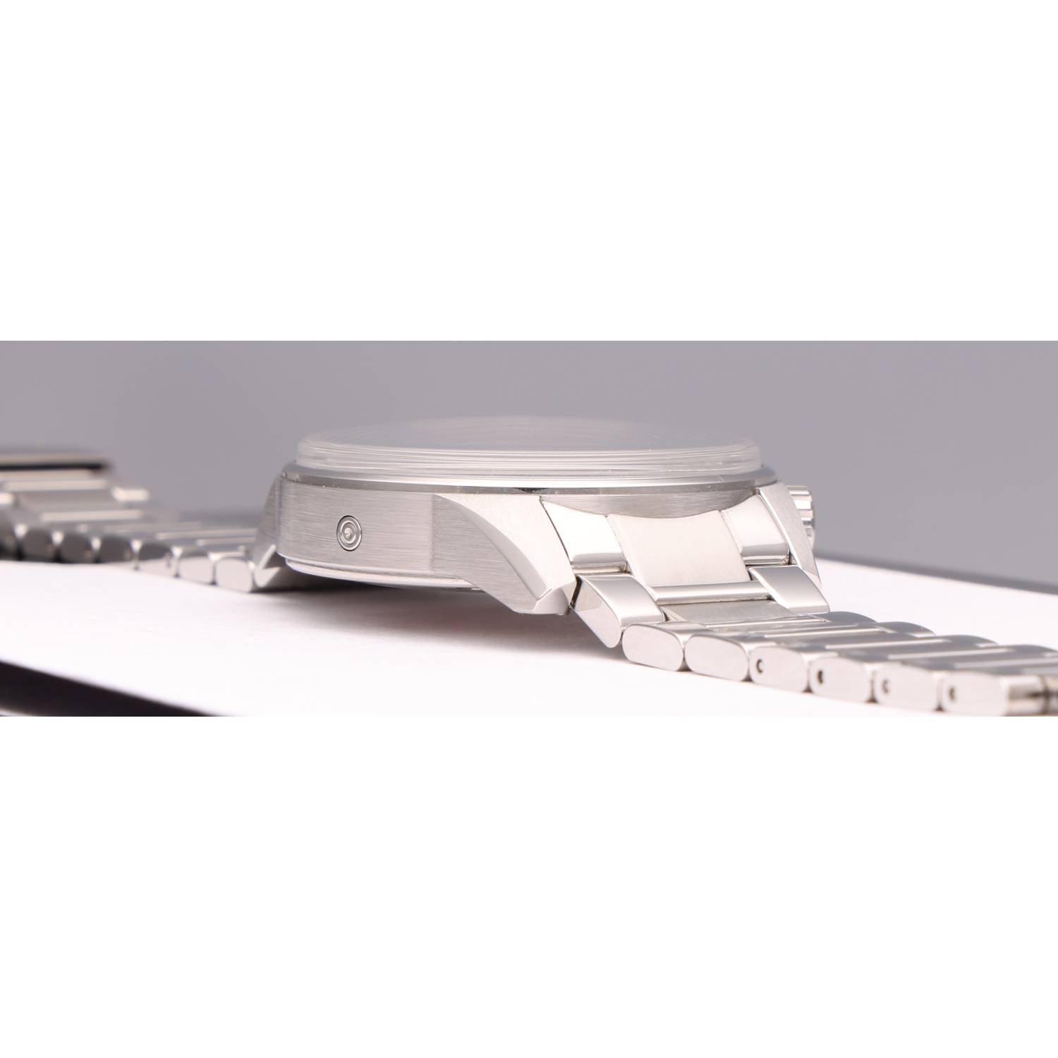 Close-up of a silver stainless steel wristwatch showing the case and linked bracelet on a white surface, side view.