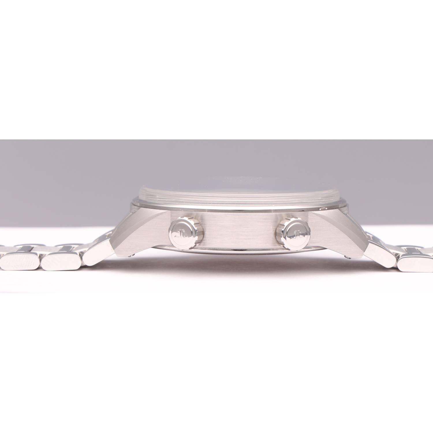 Close-up side view of a silver stainless steel wristwatch with two crown knobs and a metal bracelet on a white surface.