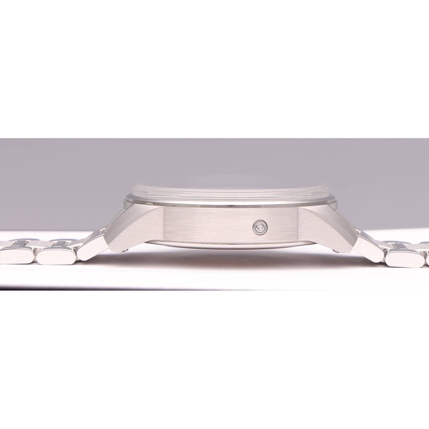 Close-up side view of a stainless steel wristwatch showing brushed case and bracelet against a light background.