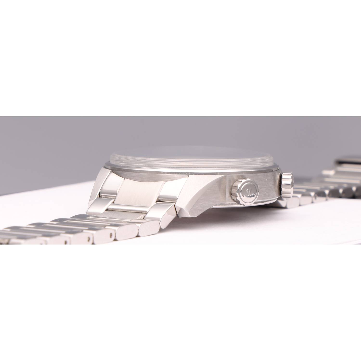 Close-up of a silver stainless-steel wristwatch lying on its side, displaying the crown and brushed case with a linked metal bracelet.