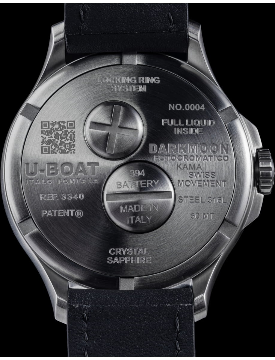 Stainless steel watch case back with engraved text, a central circular screw cap, and a black leather strap visible at the top and bottom.