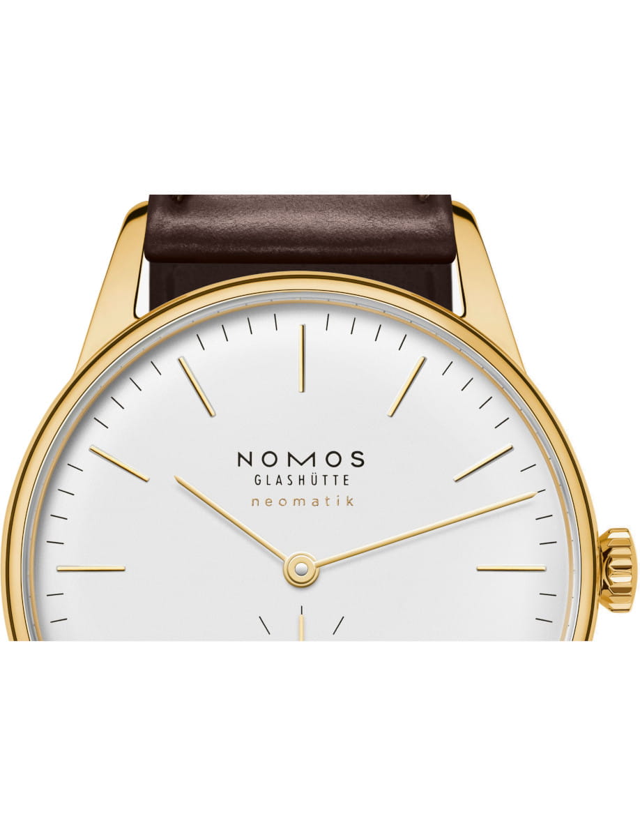 Close-up of a gold-cased Nomos Glashütte Neomatik wristwatch with a white dial and brown leather strap.
