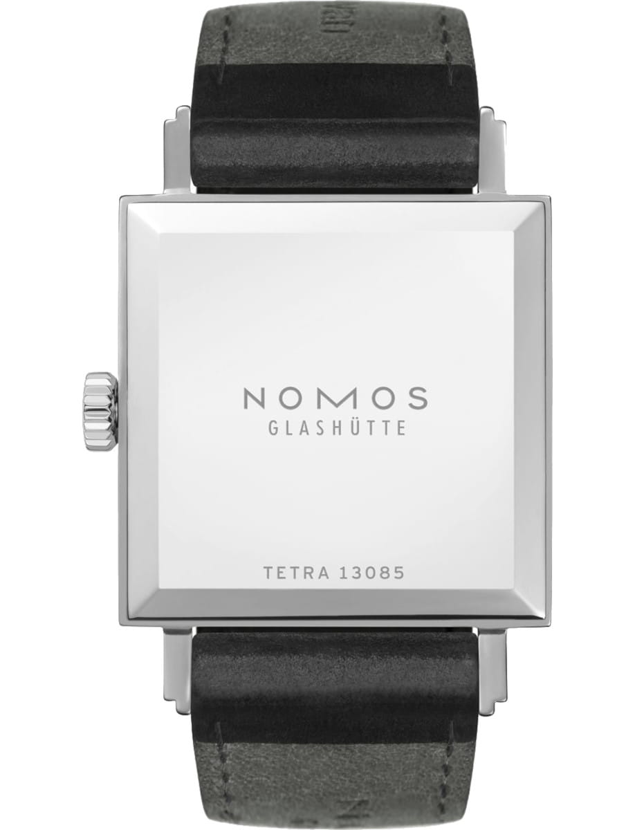 Square silver watch case with black leather strap; back case shows 'NOMOS GLASHÜTTE' and 'TETRA 13085' engravings, minimalistic design.