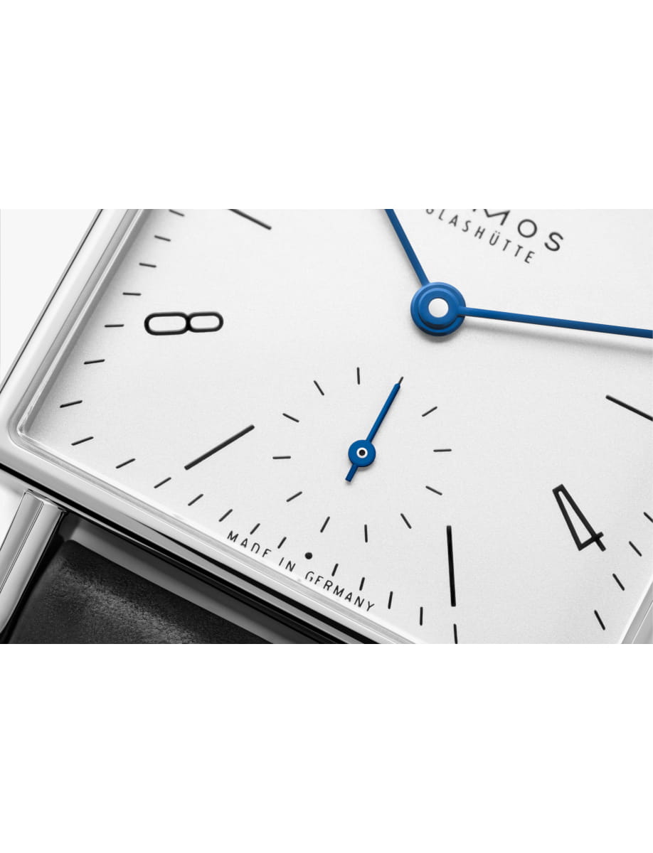 Close-up of a white watch dial with blue hour and minute hands and a small seconds subdial; 'Made in Germany' text visible.