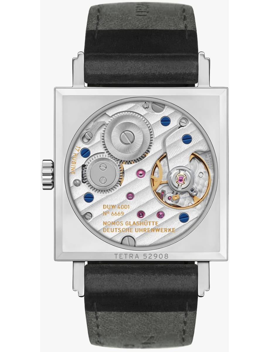 Back of a square wristwatch showing its mechanical movement with gears, screws, and blue accents; inscriptions include NOMOS GLASHÜTTE DEUTSCHE UHRENWERKE and TETRA 52908