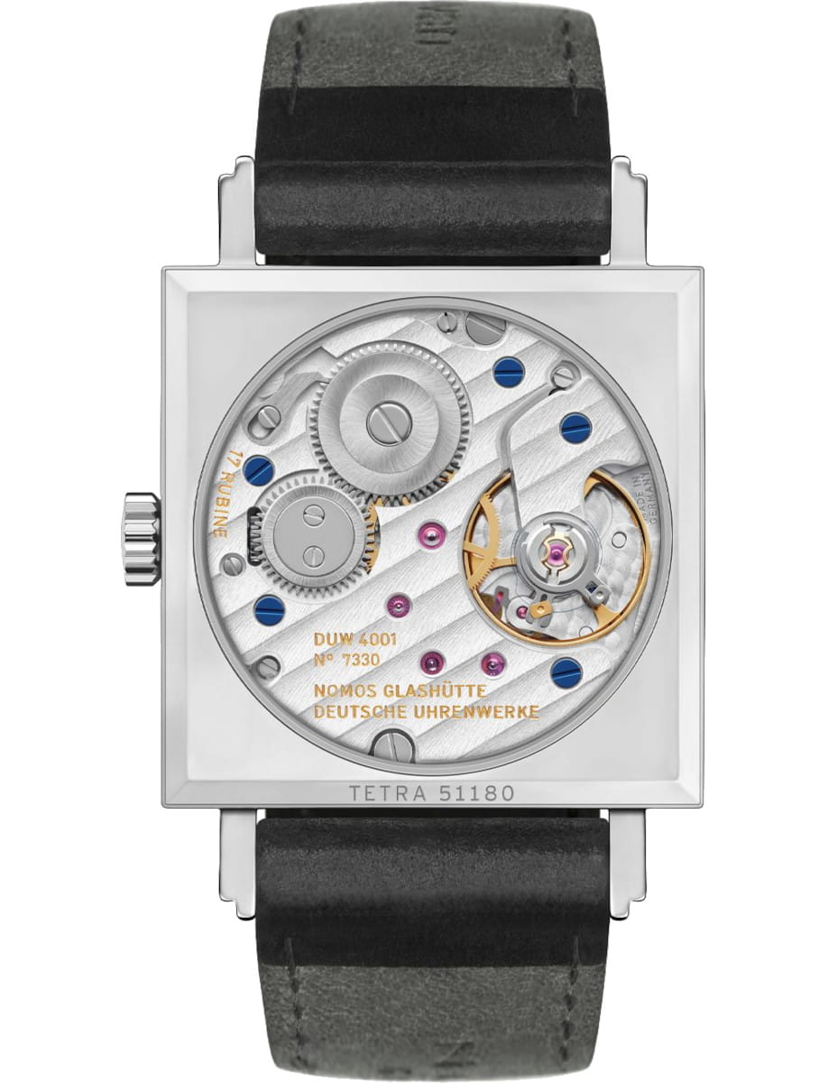 Square stainless steel watch with a transparent case back showing intricate gears, blue screws, and a leather strap; engraved movement details are visible across the plate.