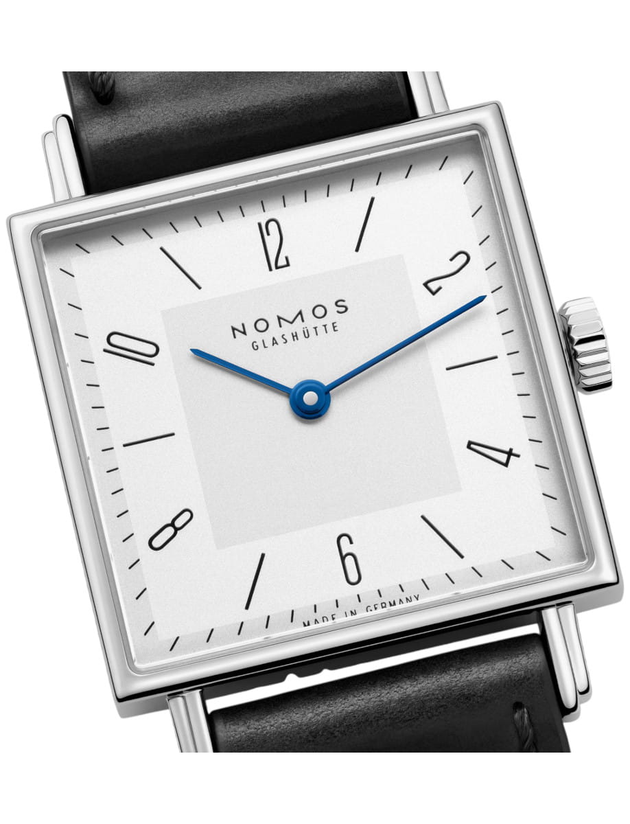 Nomos Glashütte square-faced wristwatch with a white dial, blue hands, silver case, and black leather strap