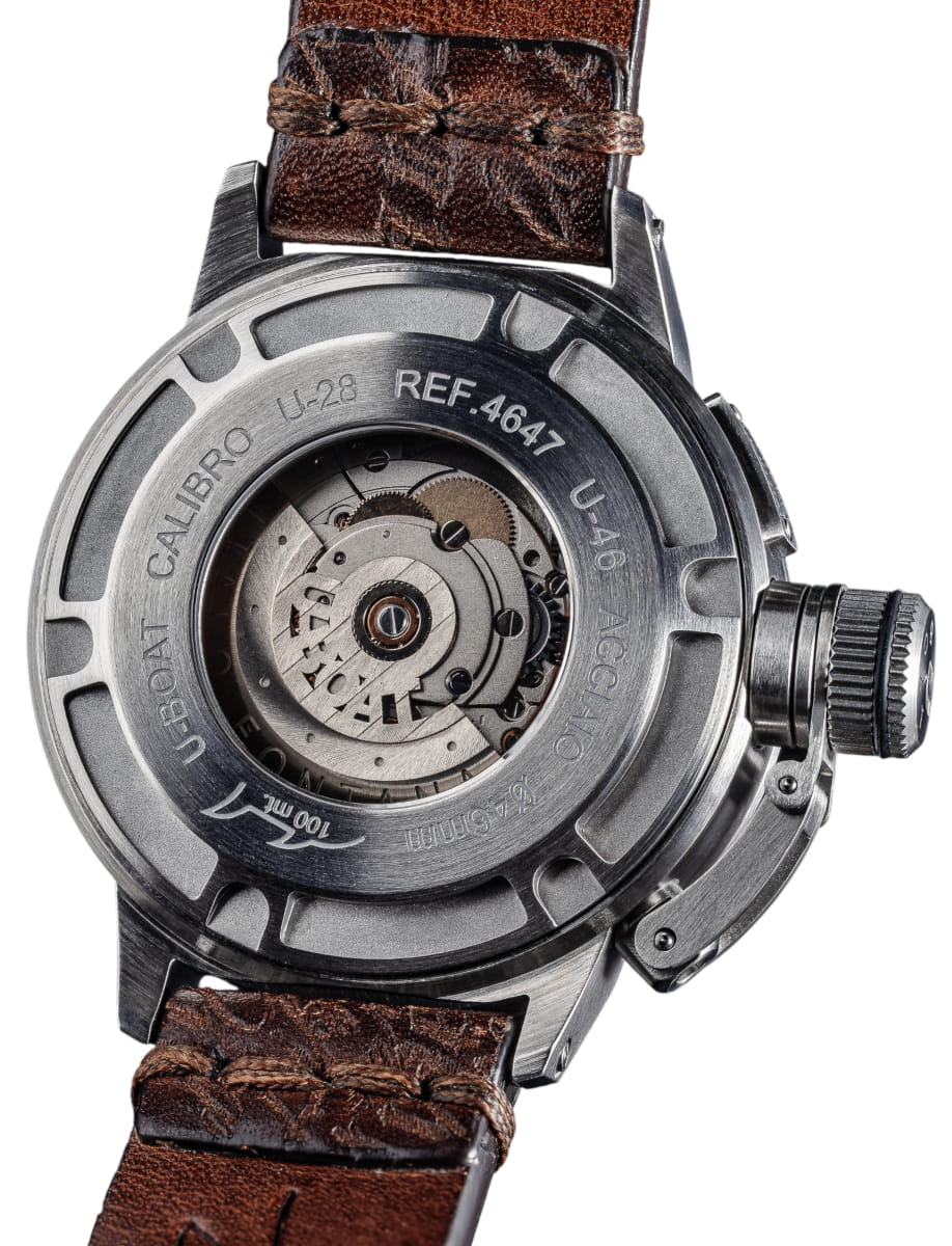 Close-up of a stainless steel watch case back with a transparent window, revealing the mechanical movement, attached to a brown leather strap.