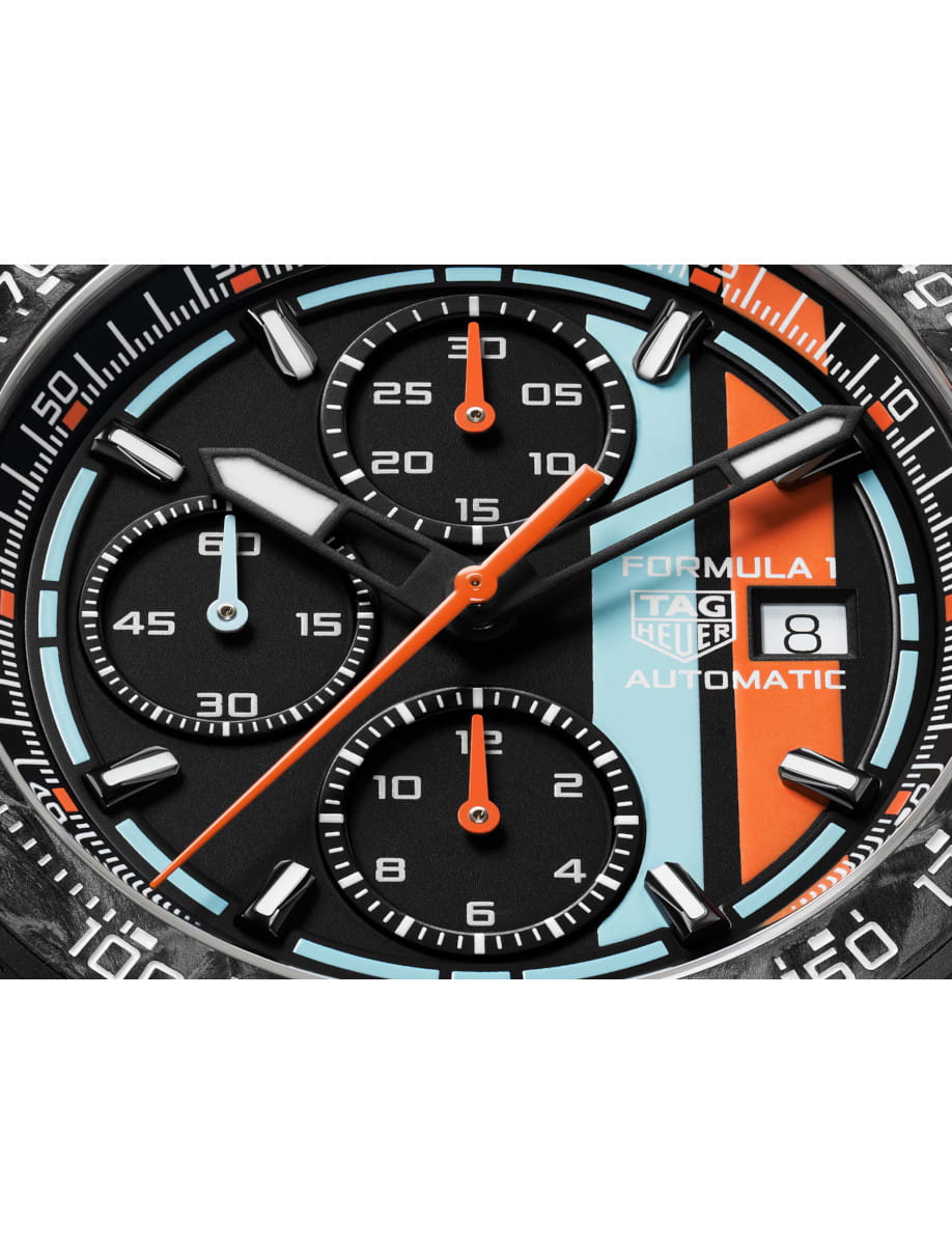 Close-up of a TAG Heuer Formula 1 chronograph watch face with turquoise and orange stripes and a date window.