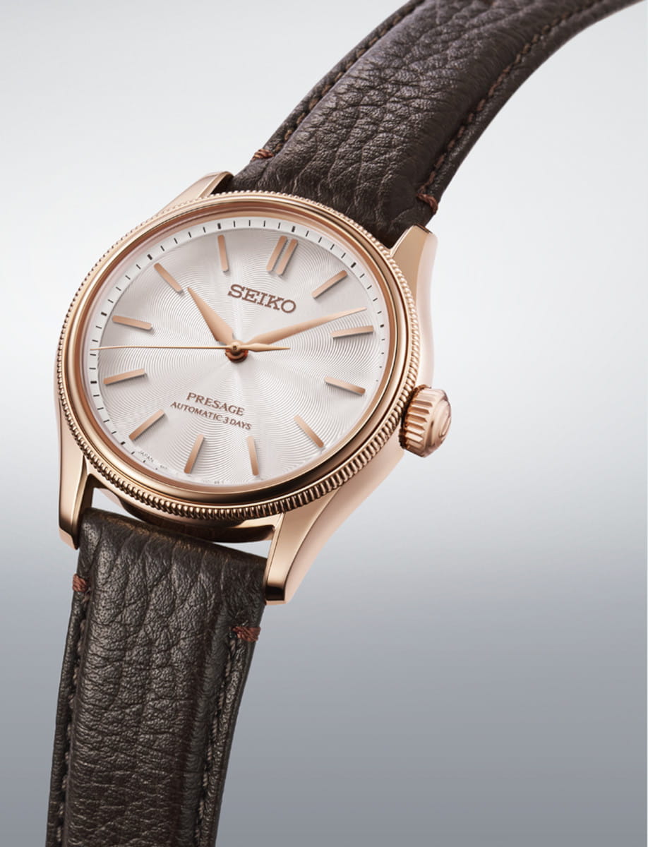 Rose gold colored stainless steel Seiko Presage wristwatch with a brown leather strap and white dial showing gold color indices and hands.