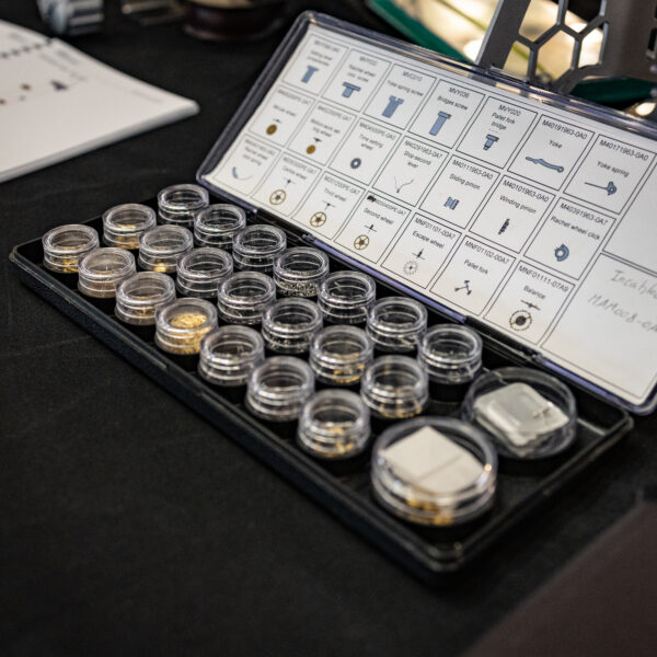 Open hardware kit with small glass jars of screws and a printed parts diagram showing labeled components to the right in a binder