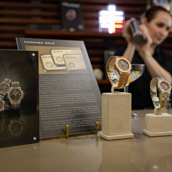 Display of gold wristwatches on beige stands at a jewelry counter, with a promotional card in the background.