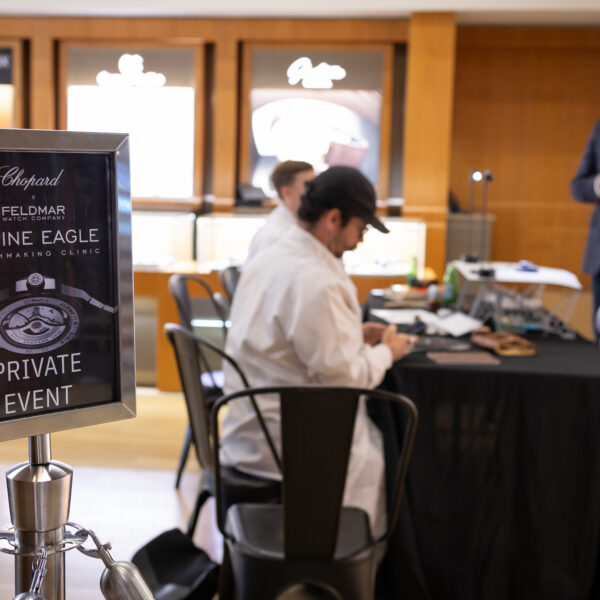 Promotional sign reading 'Chopard x FELDMAR ALPINE EAGLE WATCHMAKING CLINIC PRIVATE EVENT' in focus; blurred staff and attendees at tables in background.