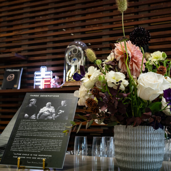 Colorful flower bouquet in a gray woven vase on a display table beside a black-and-white exhibit panel in a museum setting.