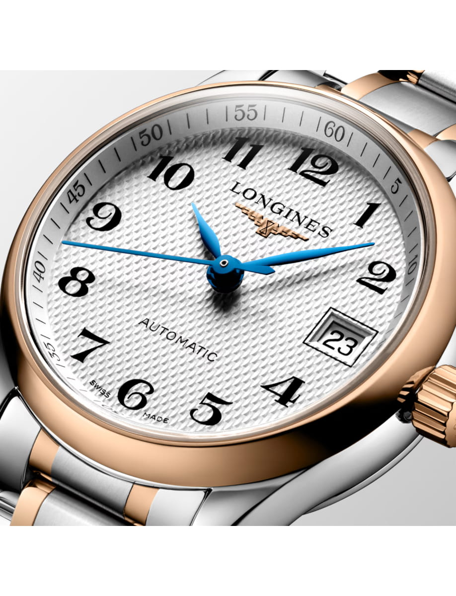Close-up of a two-tone Longines wristwatch with a silver guilloché dial, blue hands, rose-gold bezel, and a date window at 3 o'clock, marked AUTOMATIC on the dial.