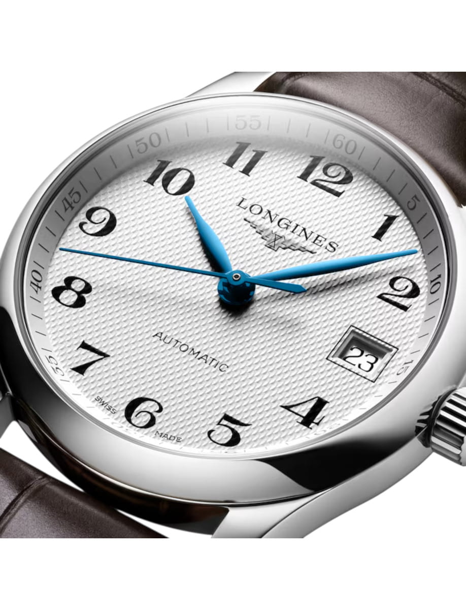 Close-up of a silver Longines automatic wristwatch with blue hands, date display showing 23, and a brown leather strap.