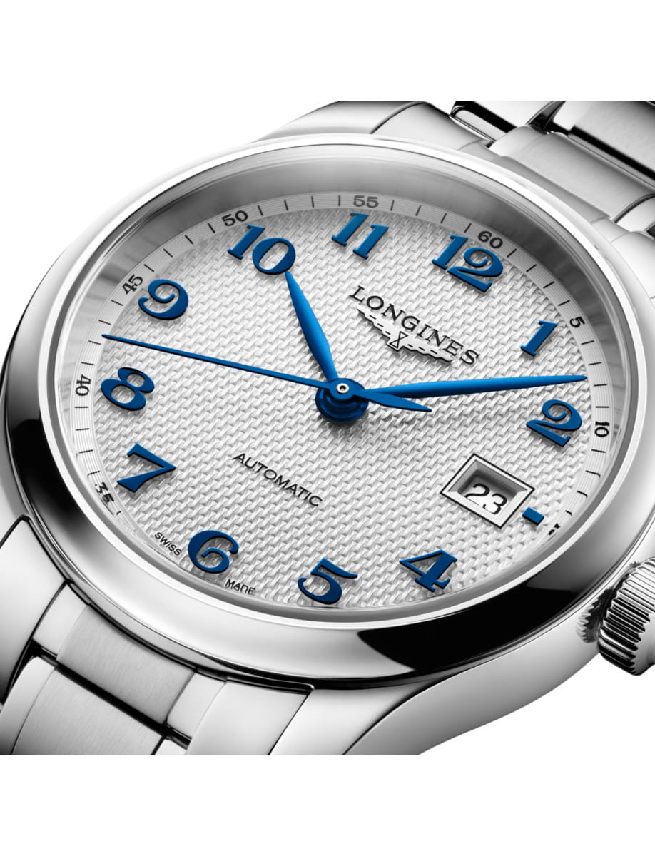 Close-up of a steel wristwatch with blue Arabic numerals and a date window at 3 o'clock on a textured dial.
