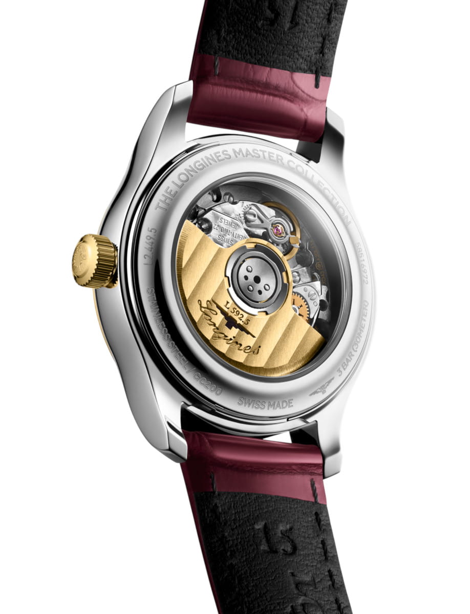 Close-up of a stainless steel watch back showing the mechanical movement with a yellow-gold rotor and engraved text, bordeaux-black leather strap visible behind the case