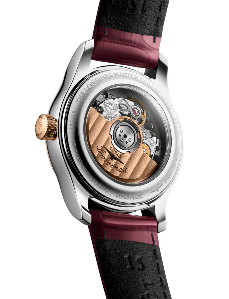 Close-up of a stainless steel watch back showing the mechanical movement with a rose-gold rotor and engraved text, bordeaux-black leather strap visible behind the case