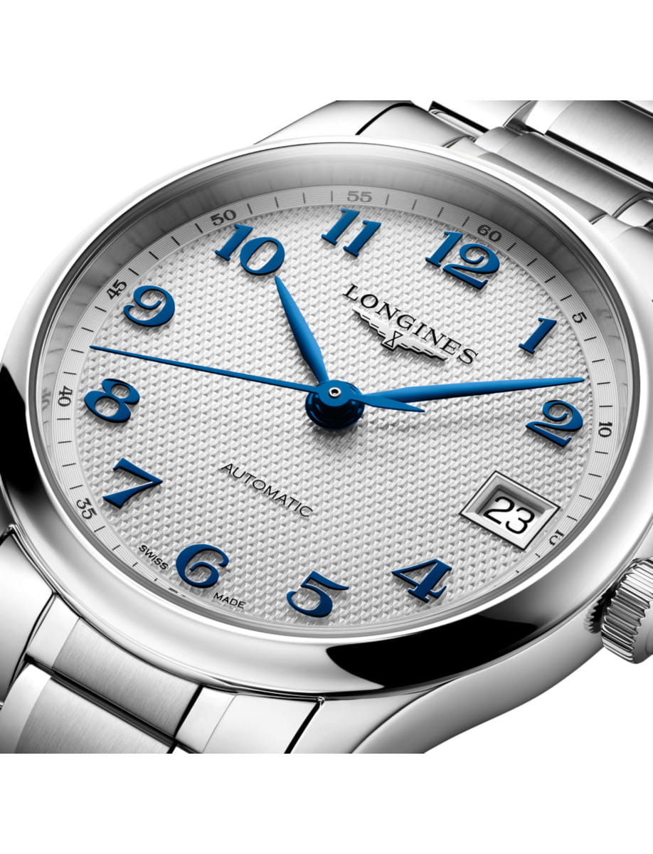 Close-up of a stainless steel Longines wristwatch with blue numerals, Silver barleycorn dial, and a date window showing 23 at 3 o'clock.