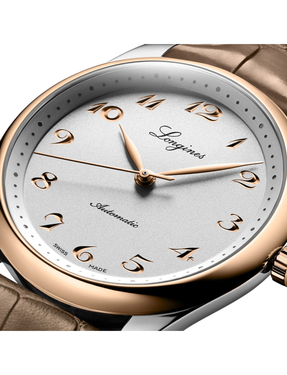 Close-up of a silver and rose-gold Longines wristwatch with a beige leather strap.