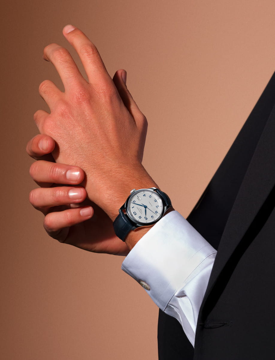 A person in a suit adjusts a silver analog wristwatch on their left wrist with a white shirt cuff showing.