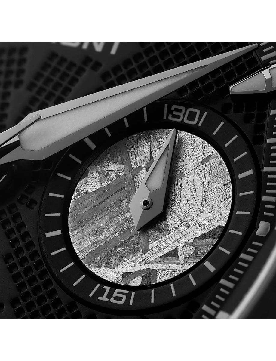 Close-up of a black bezel watch with white markers and angular metallic hands, textured cracked-pattern dial.