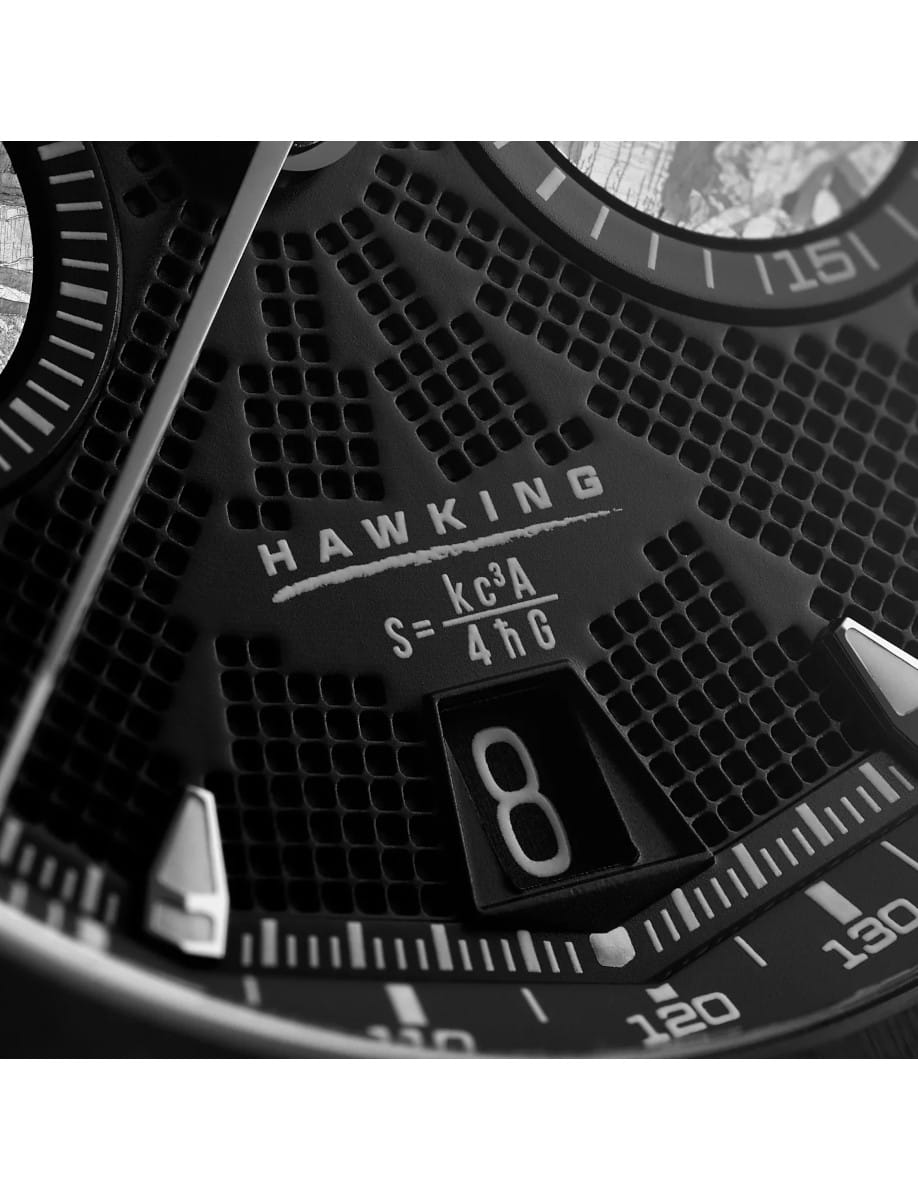 Close-up of a black watch dial showing the word HAWKING, with a date window displaying 8 and surrounding measurement marks on the bezel.