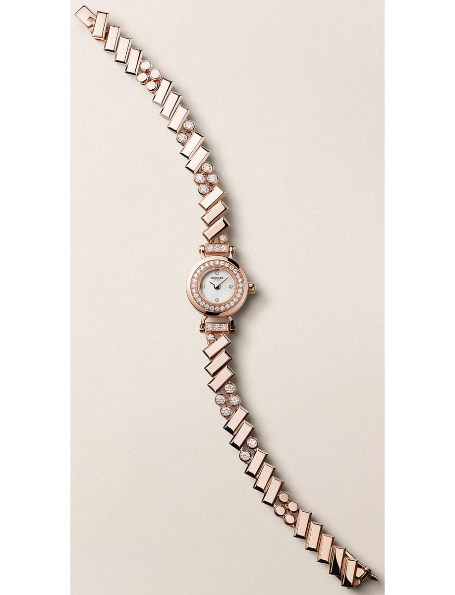 Rose gold wristwatch with a diamond-studded bezel and linked bracelet on a beige background.
