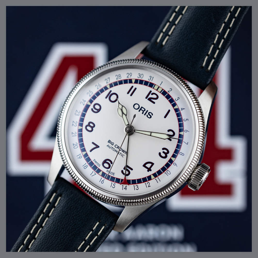 america250 10 | Feldmar Watch Co. Close-up of an Oris Big Crown automatic wristwatch with a white dial, black numerals, and blue/red bezel on a dark blue strap
