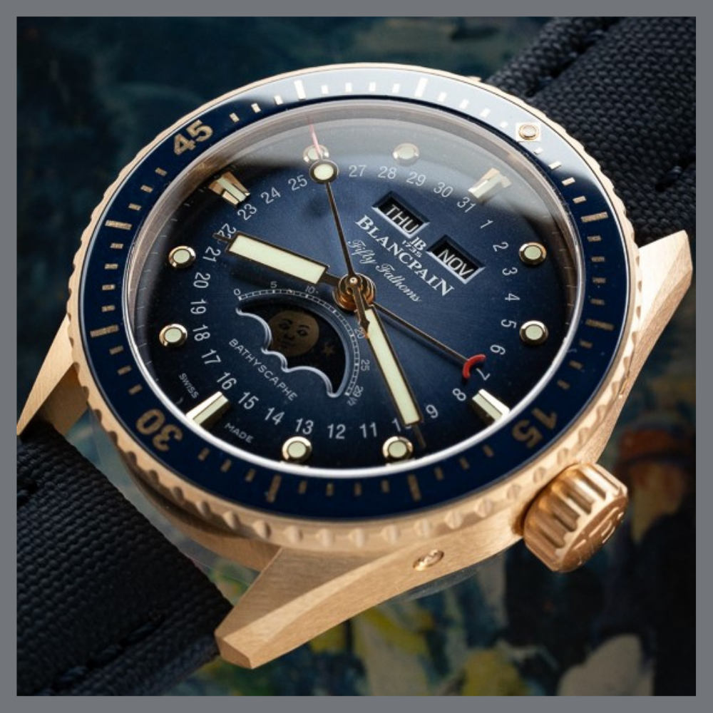 america250 9 | Feldmar Watch Co. Close-up of a gold Blancpain diver's watch with a blue dial, rotating bezel, day/date windows, and a black strap.