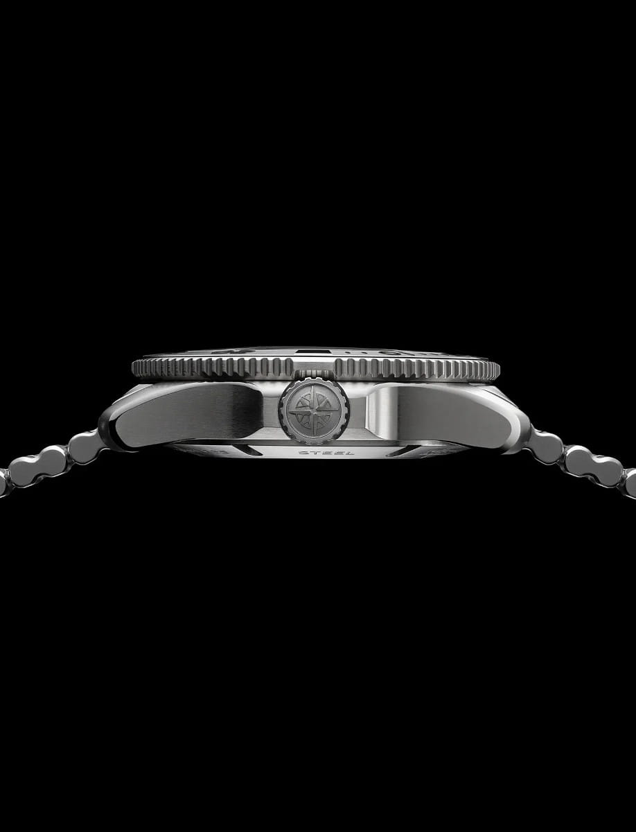Side view of a steel wristwatch with a knurled bezel and crown, metal bracelet against a black background.