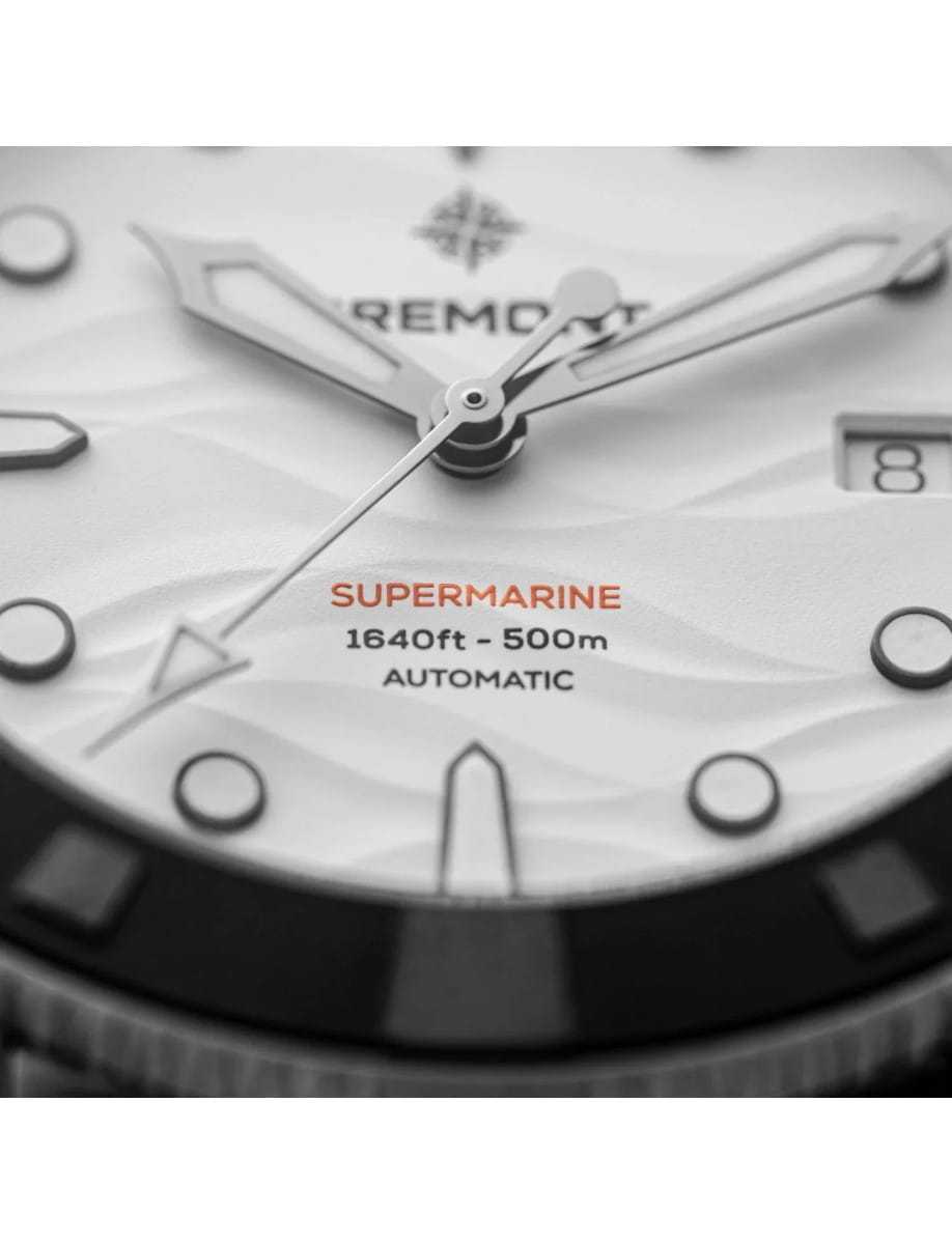 Close-up of a watch face showing the words 'SUPERMARINE 1640ft - 500m AUTOMATIC' with silver hands and a date window at 3 o'clock.