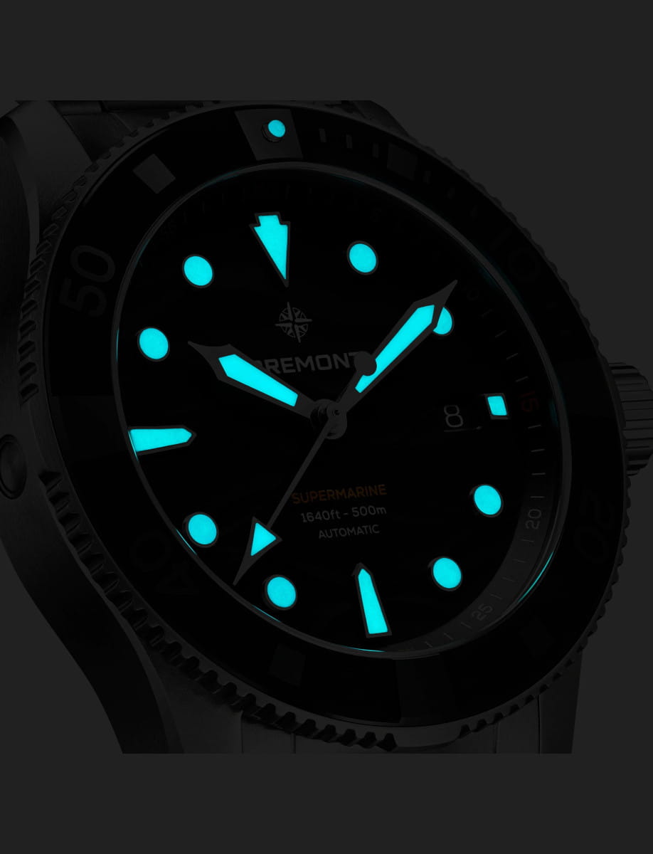 Close-up of a steel watch with blue luminous hands and markers glowing in the dark.