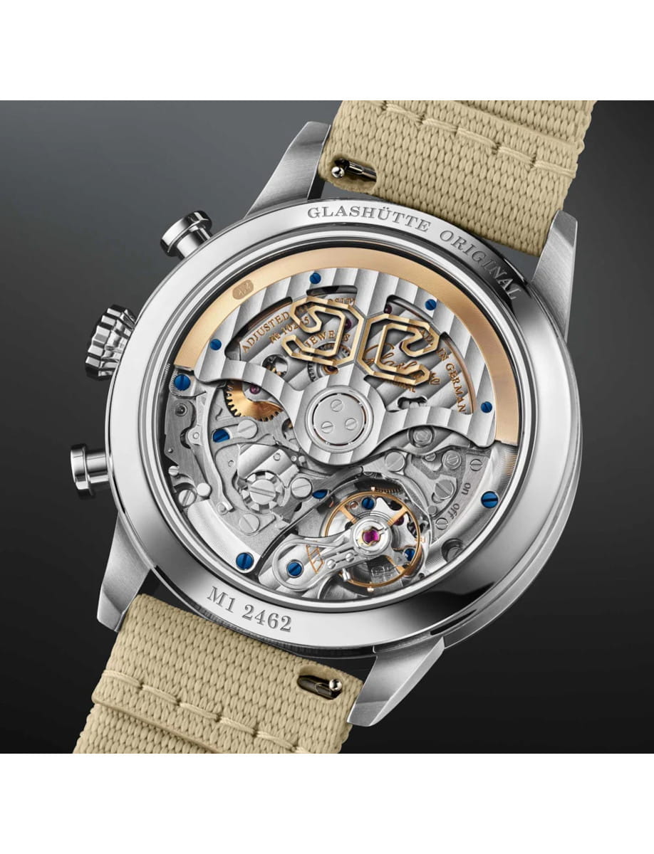 Transparent case back of a luxury wristwatch showing the intricate mechanical movement with blue screws and gold-toned bridges, beige fabric strap visible at the edges.
