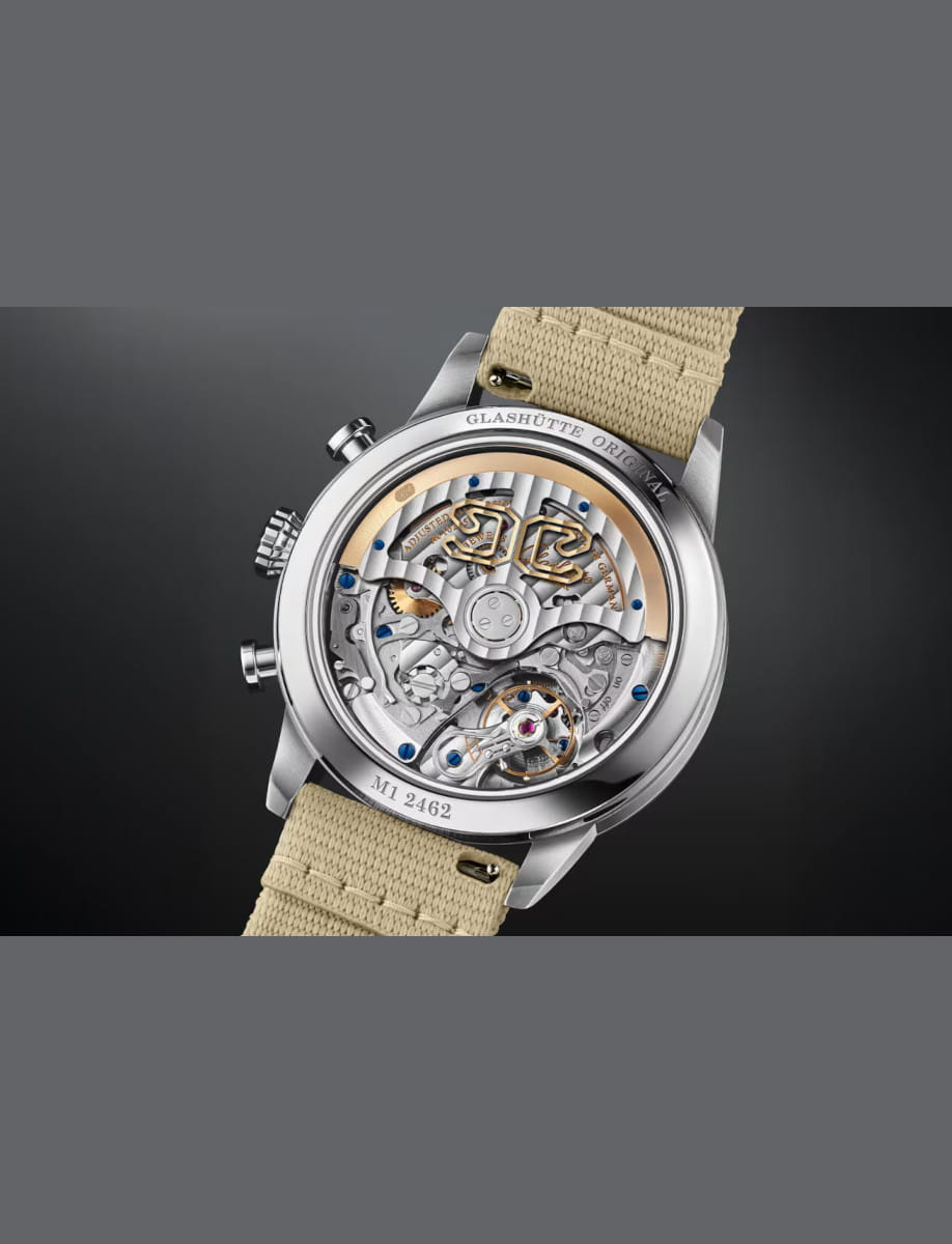 Stainless steel wristwatch with a transparent case back revealing the intricate mechanical movement and a beige fabric strap.
