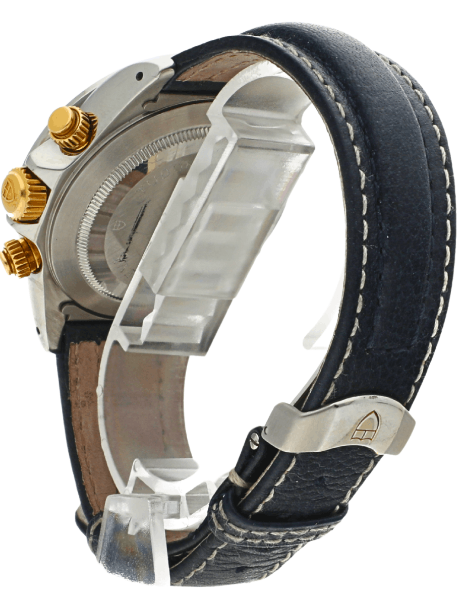 Side view of a stainless steel wristwatch with gold crowns and a dark leather strap with white stitching.