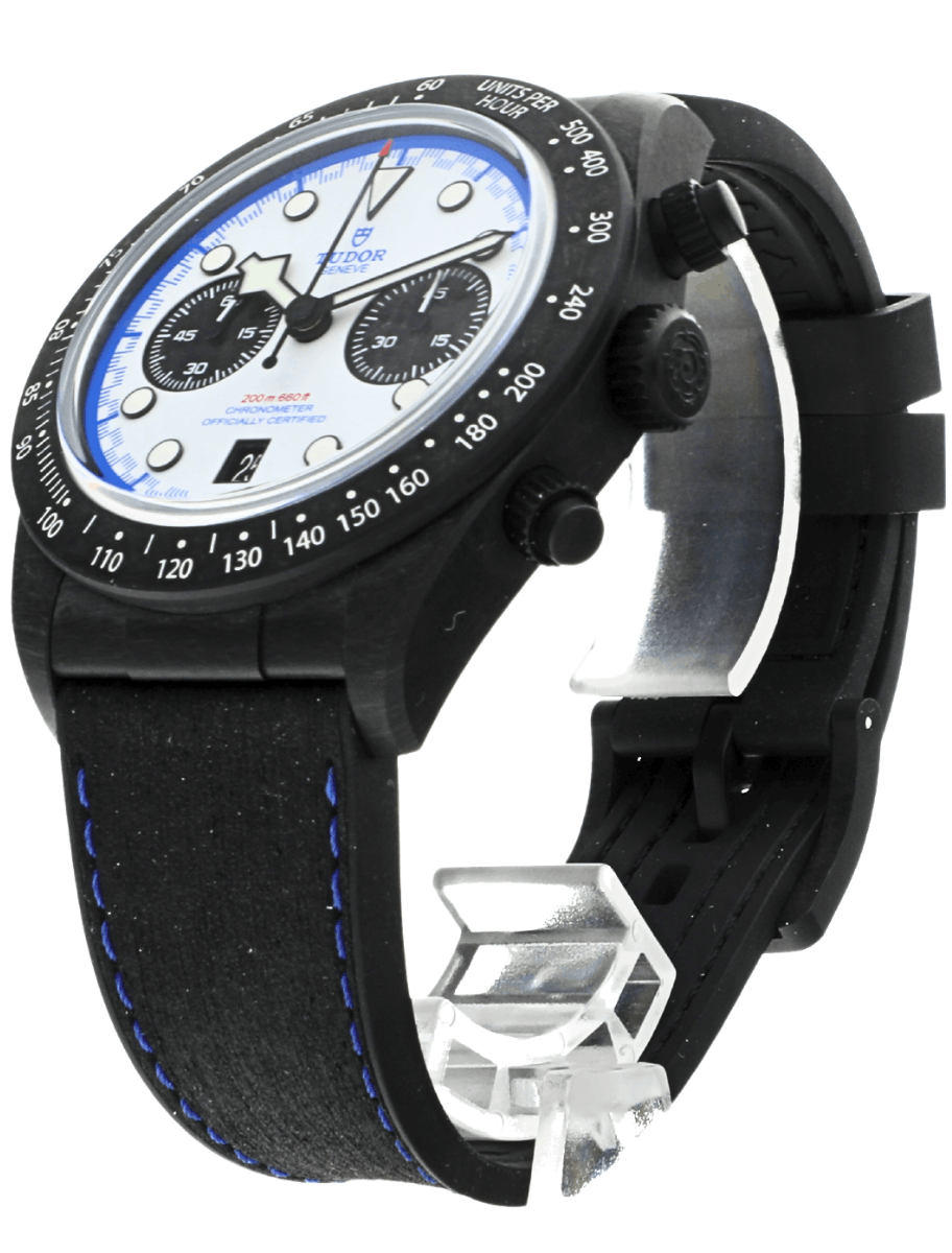 Front side view of a pre-owned Tudor carbon watch with a white dial, blue accents, two subdials, and a blue-stitched black strap.