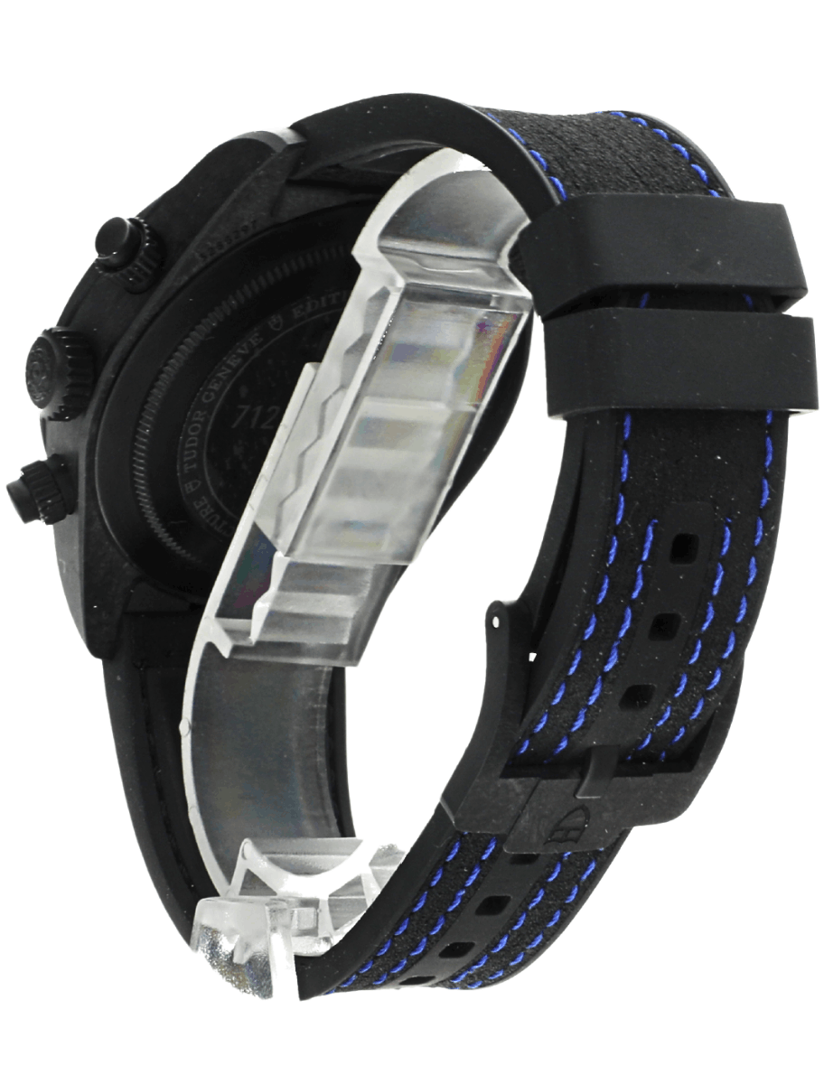 Pre-owned Tudor carbon wristwatch with blue-stitched strap and exposed metal case back.