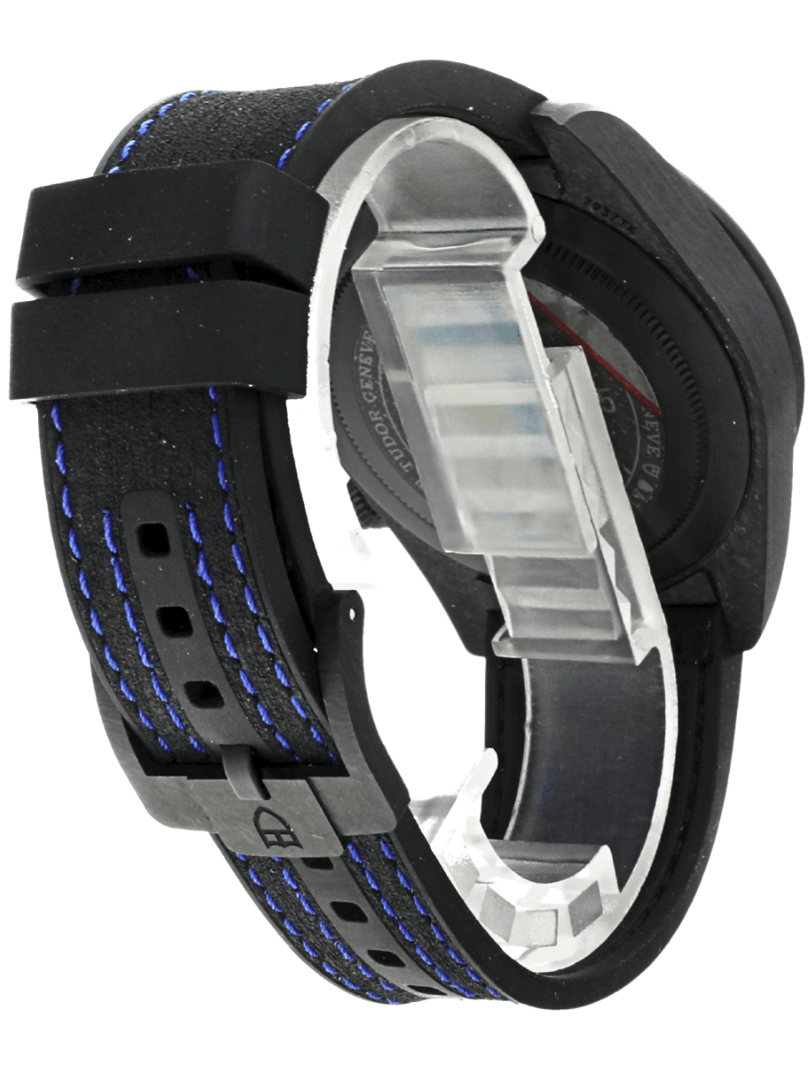Pre-owned Tudor carbon wristwatch with blue-stitched strap and exposed metal case back.