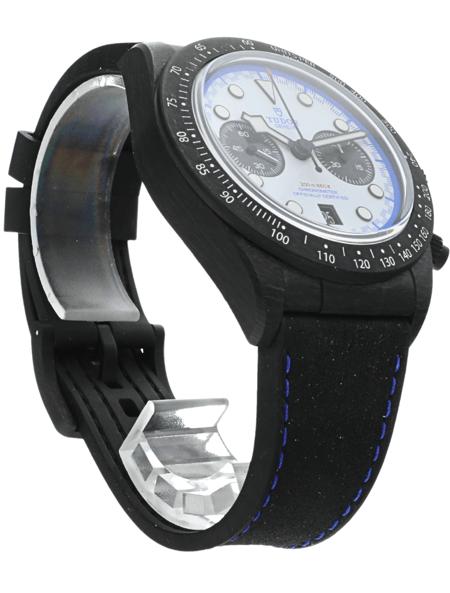 Front side view of a pre-owned Tudor carbon watch with a white dial, blue accents, two subdials, and a blue-stitched black strap.