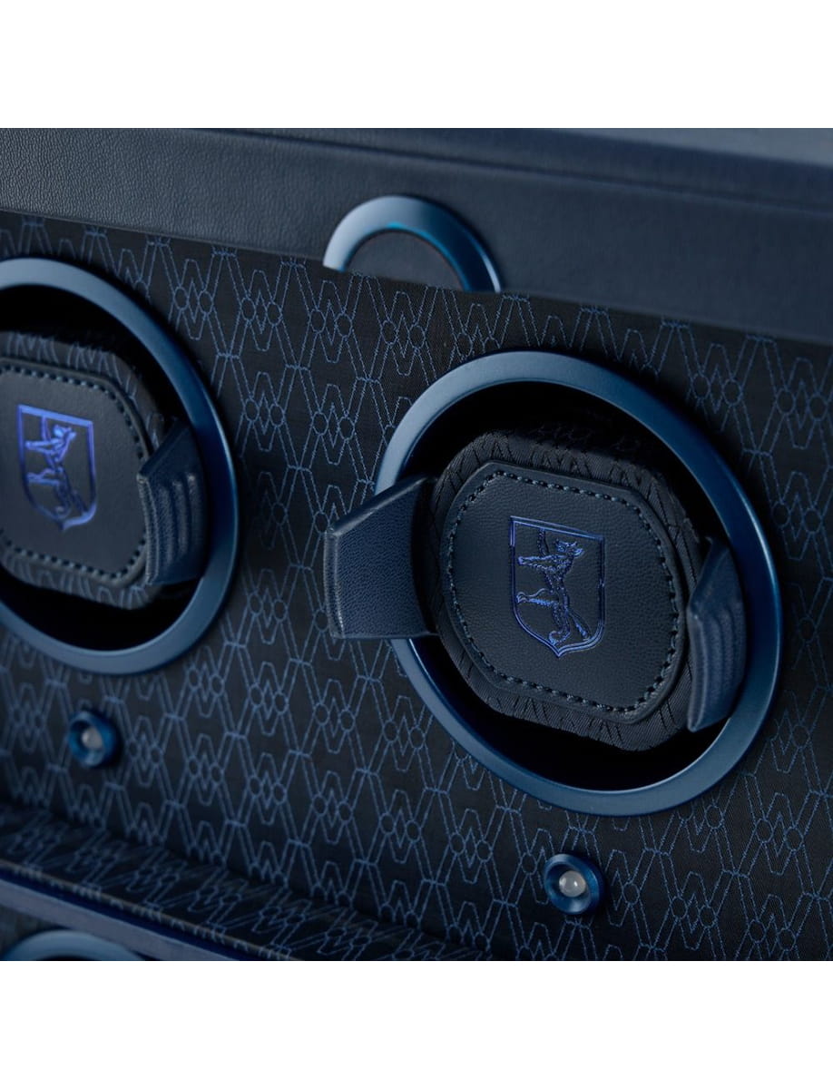 Blue over-ear headphones with a crest logo resting in a textured blue panel area of a device panel.