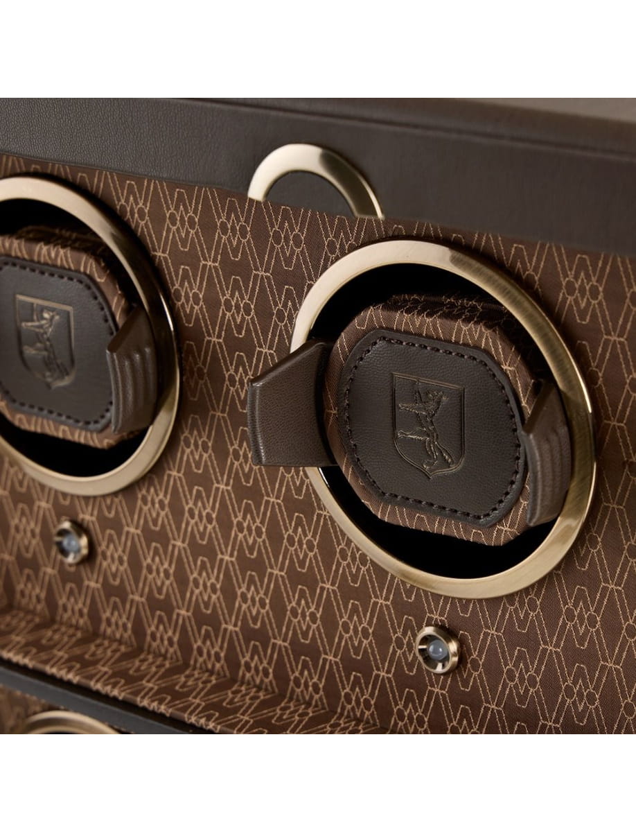 Close-up of a brown patterned suitcase with gold circular lock rings and black leather pull tabs.