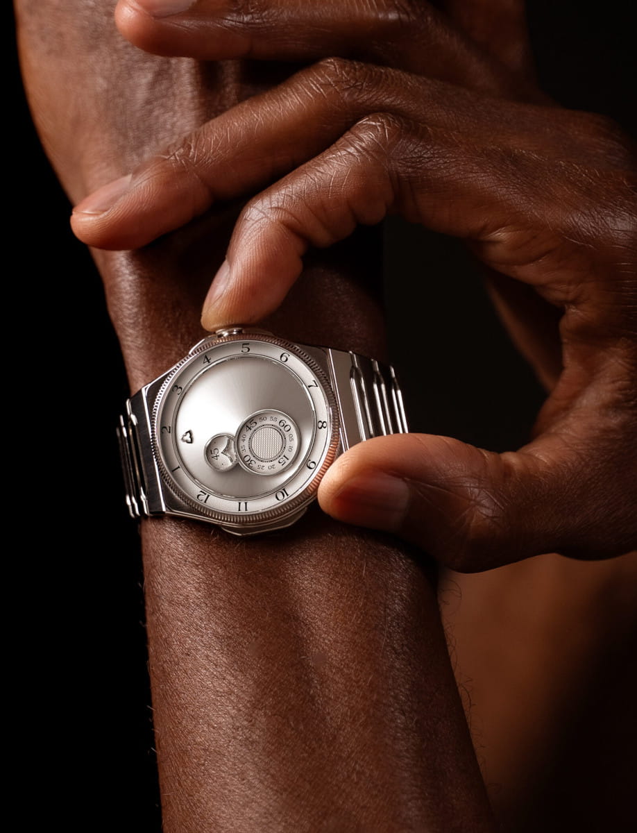 Close-up of a silver wristwatch being adjusted on a dark-skinned wrist.