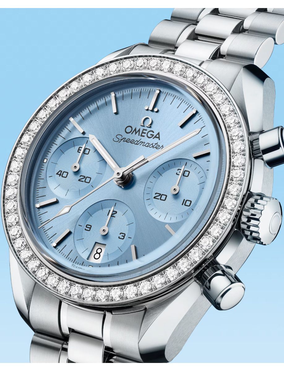 Close-up of a silver Omega Speedmaster wristwatch with a diamond-encrusted bezel and light blue dial against a blue background.